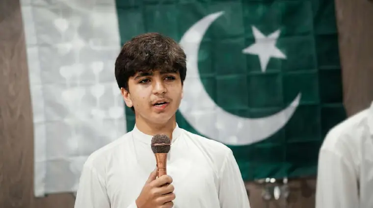 KISI student speaking into a microphone in front of the Pakistan flag during a student event