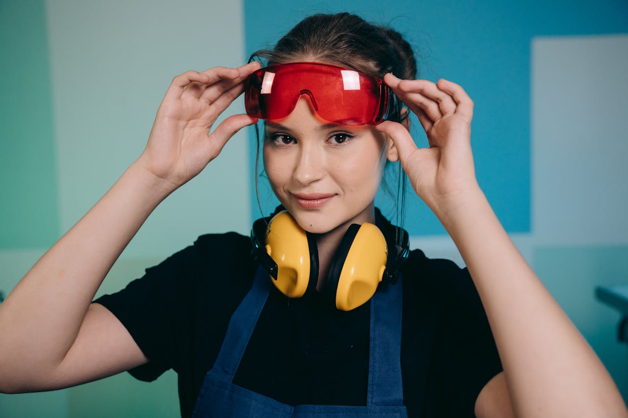 Smiling woman adjusting safety goggles with headphones, indoors setting.