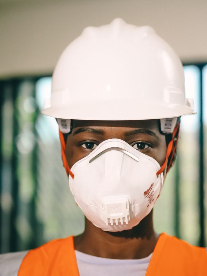 Close-up of a construction worker wearing a white hardhat and N95 mask indoors.